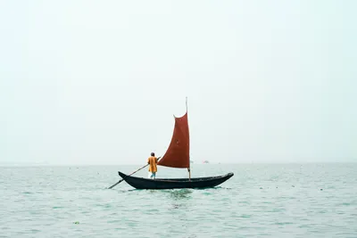 Мужчина гребет на маленькой лодке с парусом · Бесплатные стоковые фото