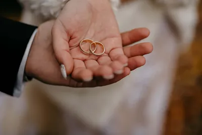 Фото рук молодоженов с кольцами на фоне свадебного платья