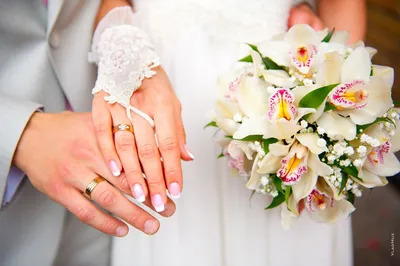 Руки молодоженов с кольцами на фоне свадебного торта