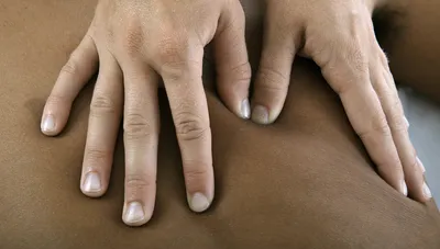 Фотография массажистских рук на фоне камня