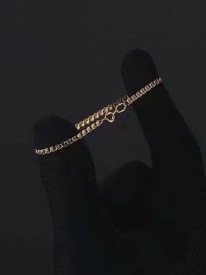 Фотография женской руки с золотым браслетом на темном фоне